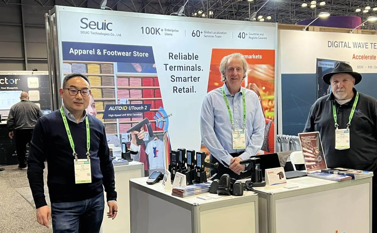 Professionals at the Seuic booth during a trade show, discussing the AUTOID UTouch 2 handheld terminal and smart retail solutions.